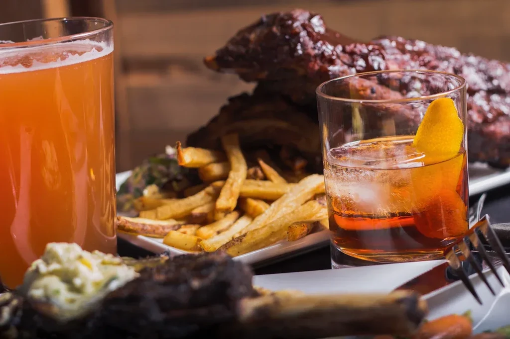 Beer, cocktail, french fries, and BBQ ribs on a table.