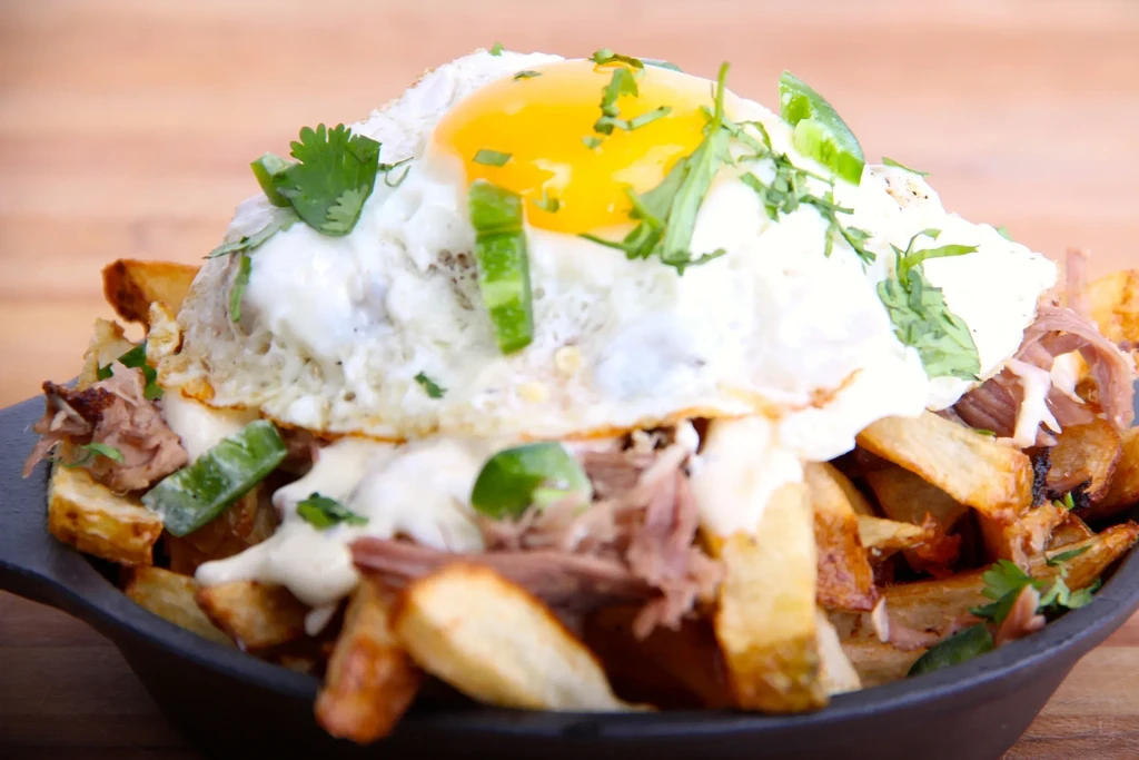 Loaded fries with shredded meat, creamy sauce, a fried egg, and greens.