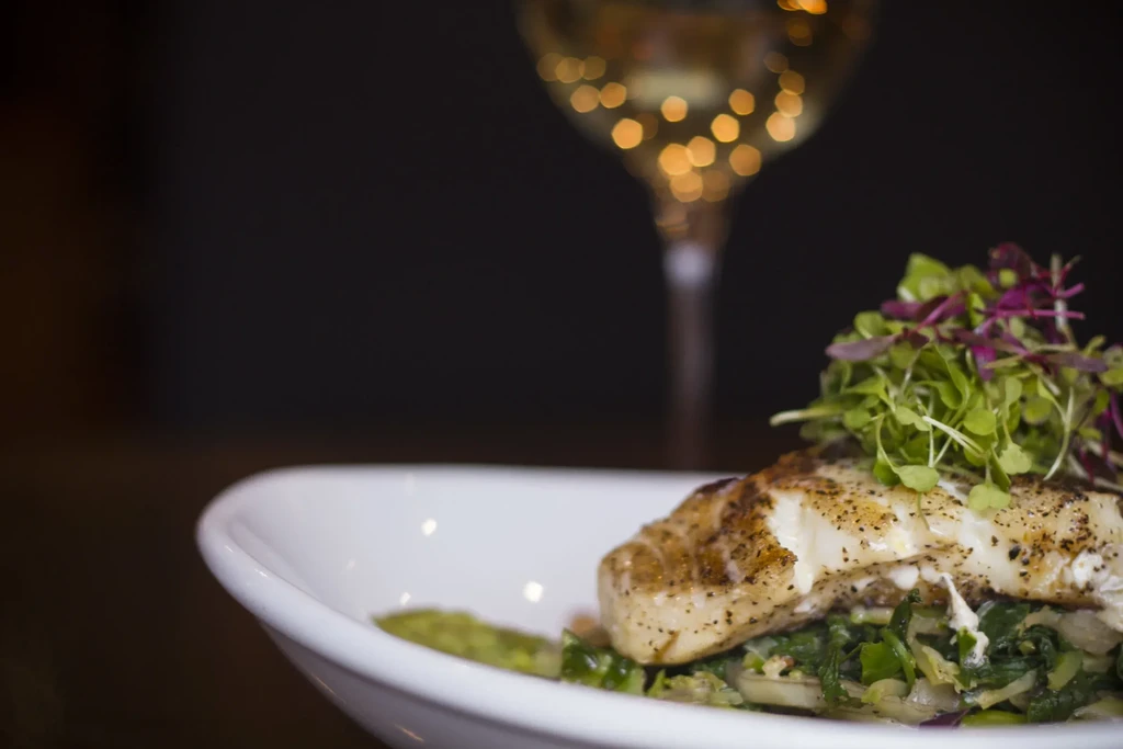 Seared white fish on green vegetables with microgreens in a bowl.