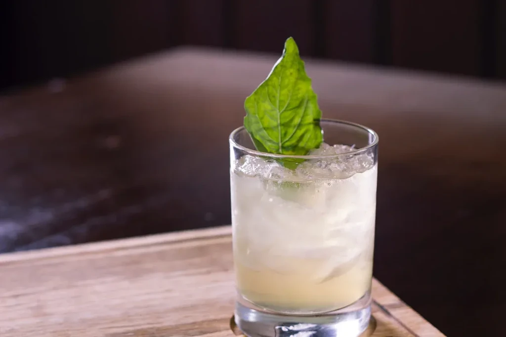 Close-up of a pale cocktail with crushed ice and an upright green leaf.