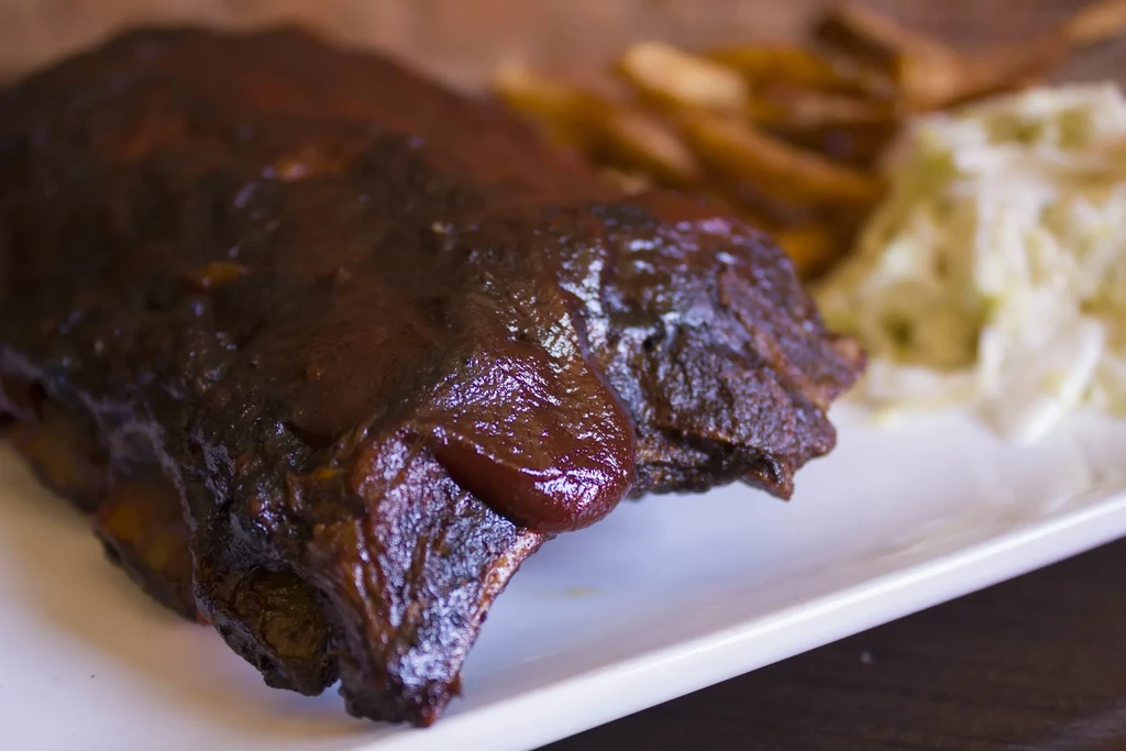 Close-up of barbecued ribs with glossy sauce, french fries, and coleslaw.