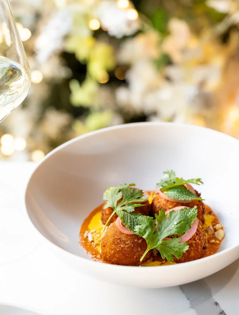 Three golden croquettes in orange sauce, herbs and onion.