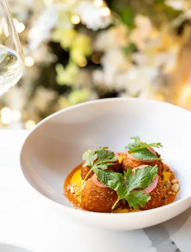 Three crispy golden items with yellow sauce, herbs, and pickled onion.