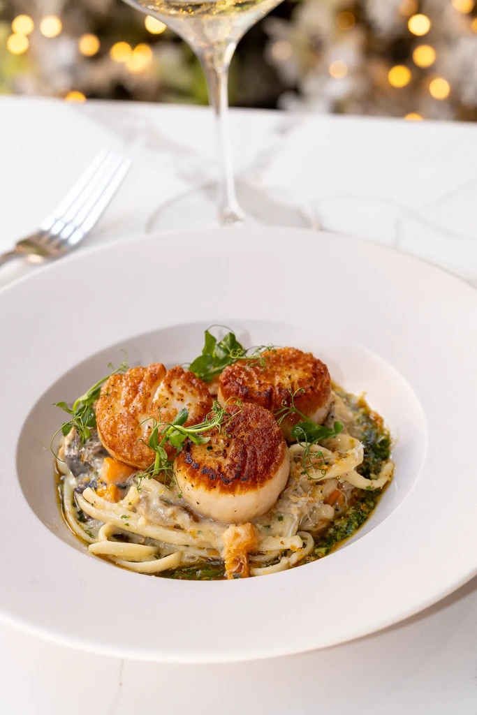 Seared scallops on pasta with creamy sauce, vegetables, and microgreens.