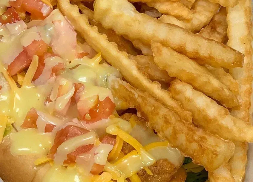 Close-up of loaded hot dog with cheese, tomato, and crinkle fries.