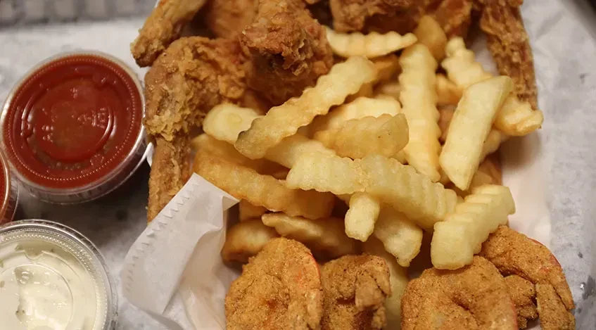 Take-out container with fried crinkle fries, breaded items, and two sauces.