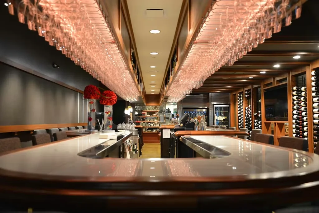 Hanging wine glasses, extensive racks in upscale, warmly lit bar.
