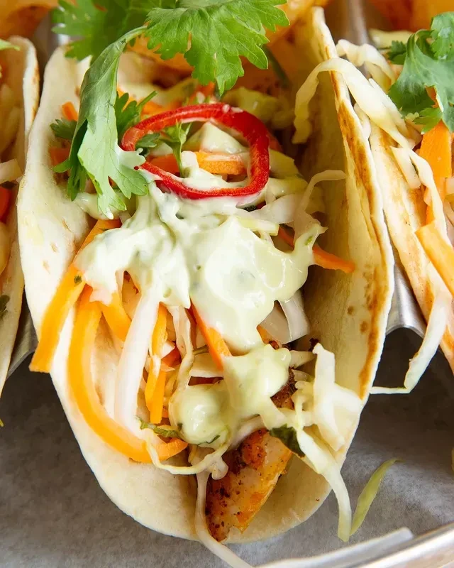 Close-up taco filled with protein, cabbage, carrots, green crema, cilantro.