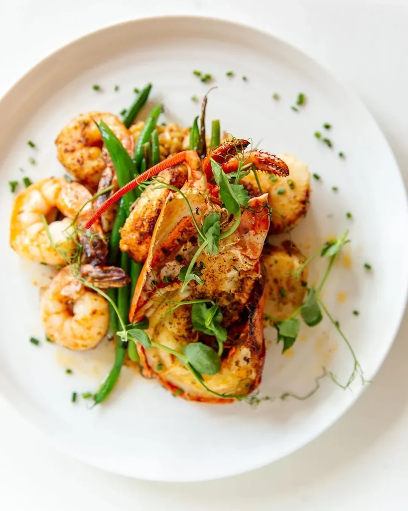 Grilled lobster, shrimp, green beans, and scallops on white plate.