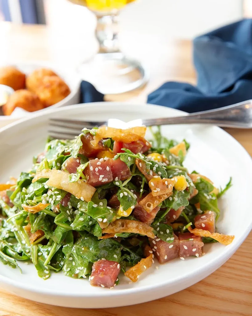 Arugula salad with tuna, yellow pieces, crispy wontons, and sesame seeds.