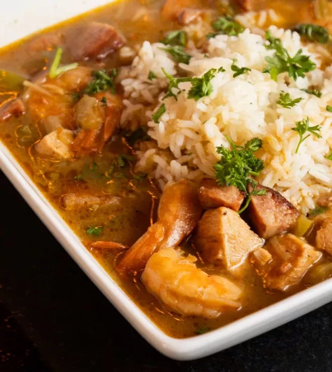 A reddish-brown gumbo with shrimp, sausage, rice, and parsley.