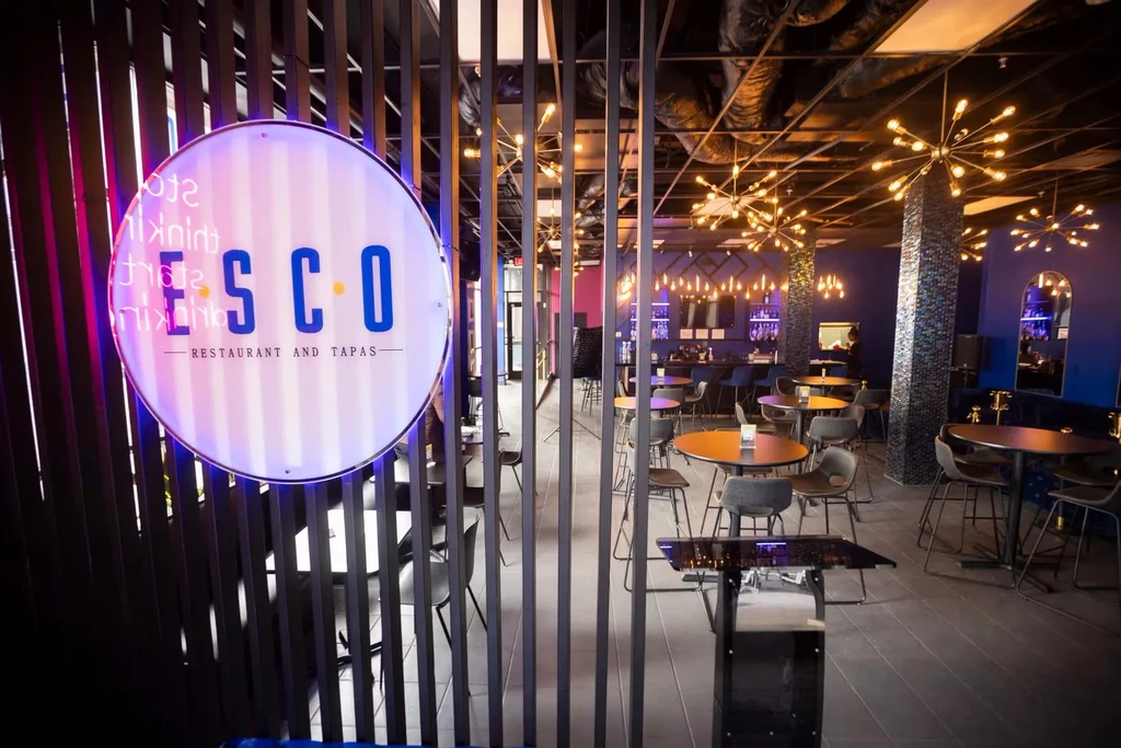 Modern ESCO restaurant with pink/blue neon sign and stylish bar.
