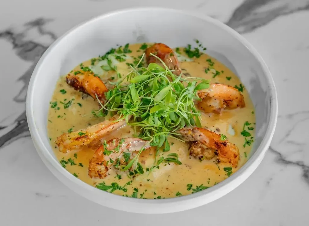Five grilled shrimp in creamy sauce garnished with green microgreens.