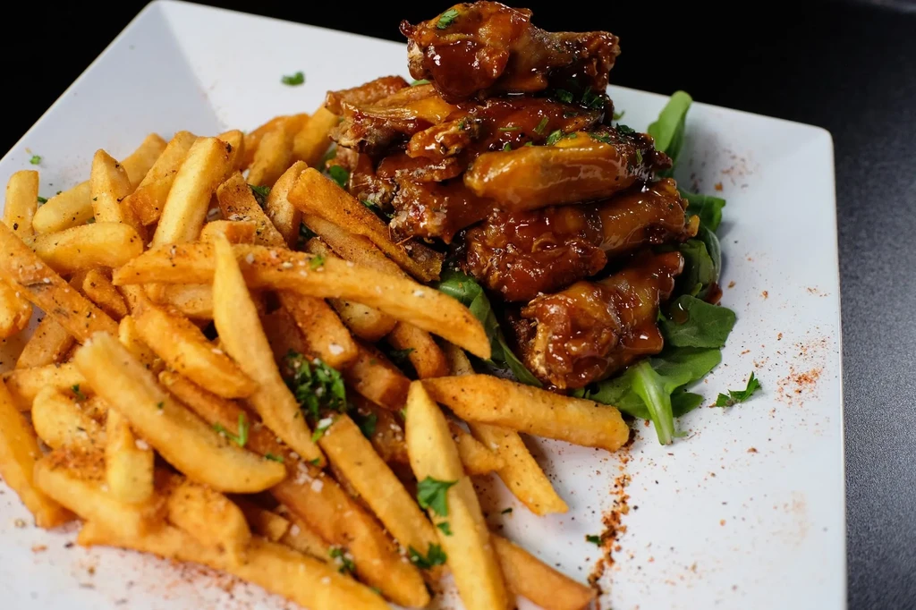 Golden french fries, glazed chicken wings, and greens on a white plate.