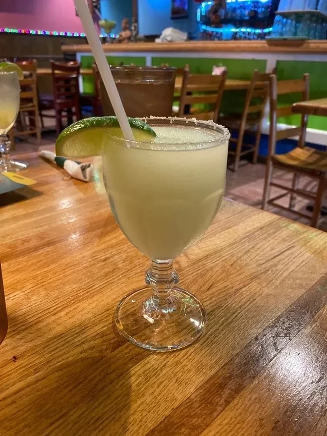 Salted frozen margarita with lime on a table, blurred restaurant background.