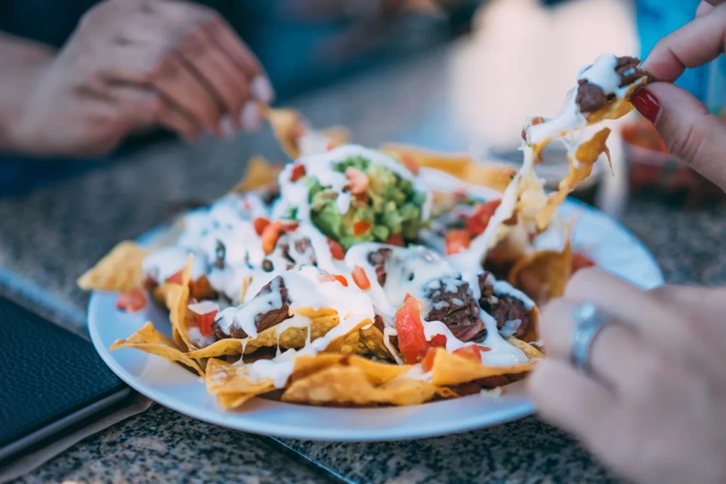 Loaded nachos with meat, cheese, guacamole, tomatoes; hands pull chips.