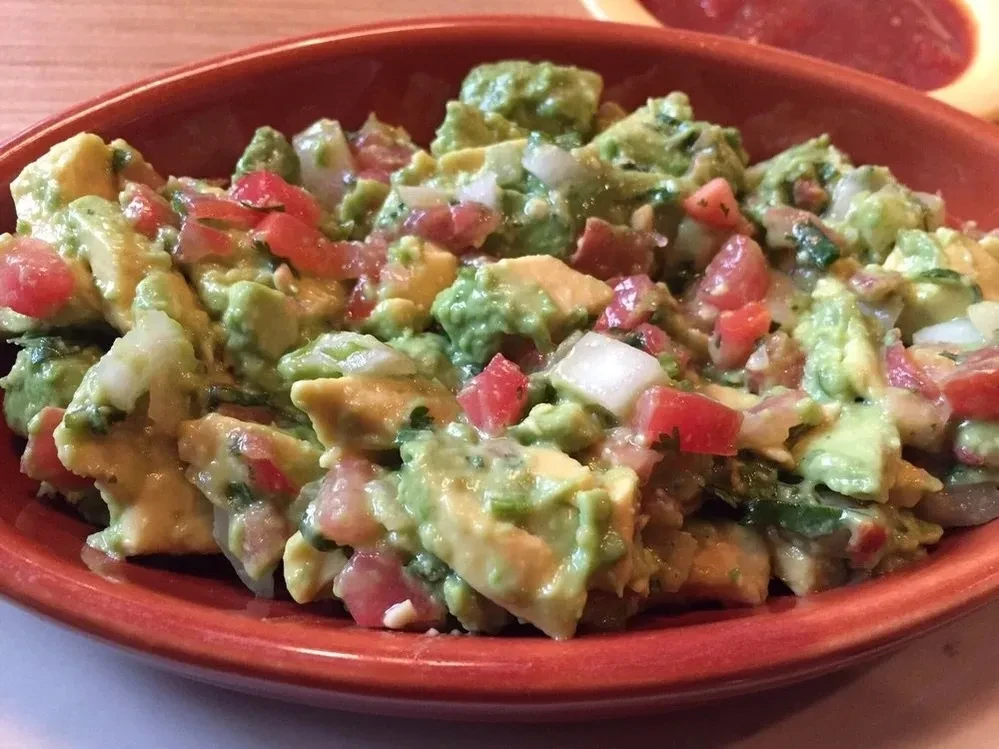 Vibrant chunky guacamole in rustic bowl, with salsa nearby.