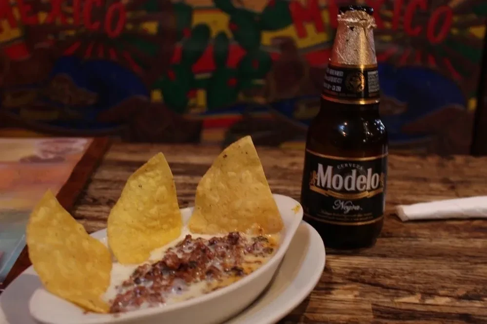 Queso fundido with tortilla chips and Modelo Negra beer on a wooden table.