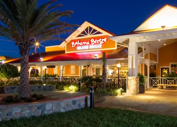 Brightly lit Bahama Breeze tropical restaurant exterior at dusk.