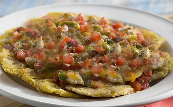 Plantain base topped with shredded meat, cheese, tomatoes, peppers, and herbs.