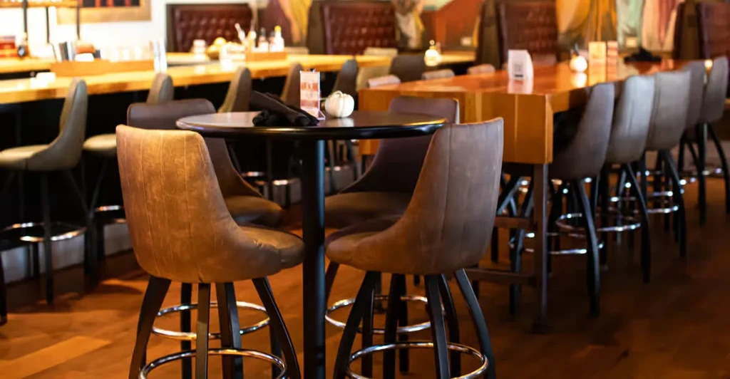 Empty restaurant with warm-toned high-top tables, bar stools, and booths.