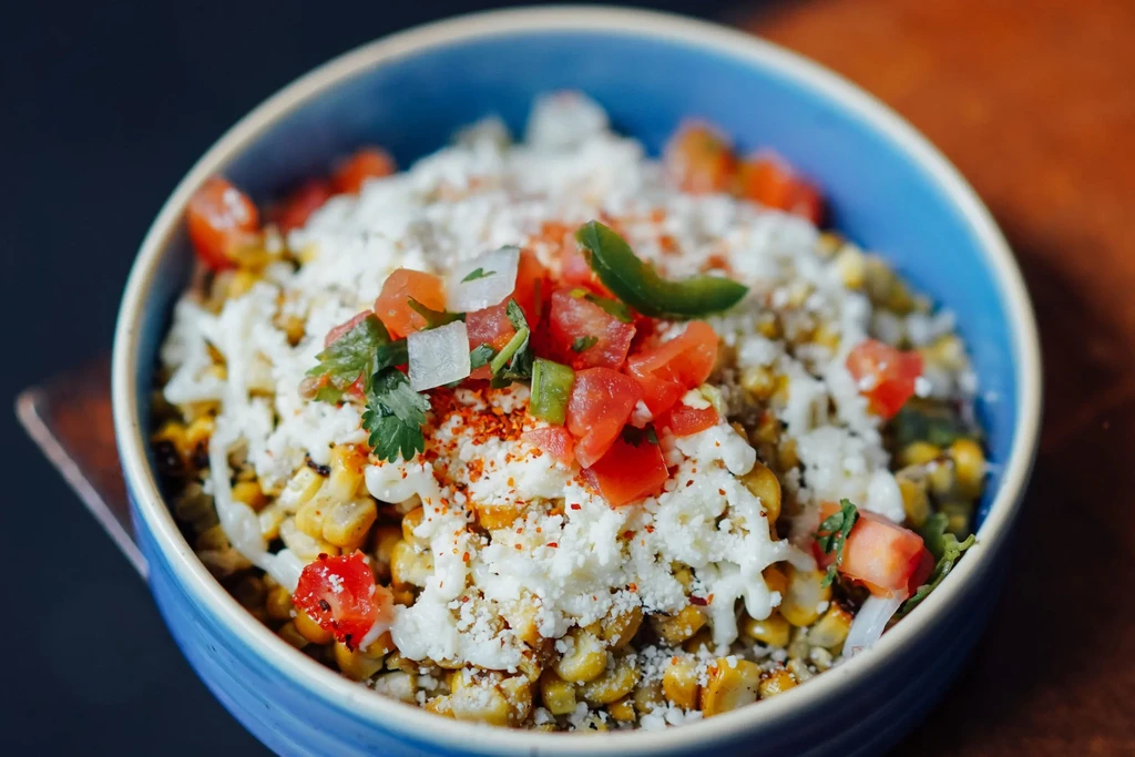 Close-up of a bowl of Esquites with corn, cheese, tomatoes, and cilantro.