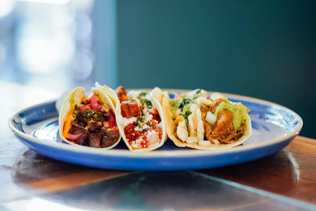 Three gourmet tacos with diverse fillings on a patterned plate.