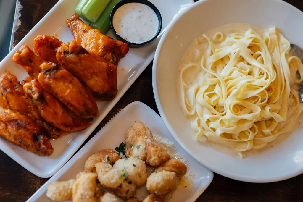 Flat lay of chicken wings, creamy pasta, and cheesy garlic knots.