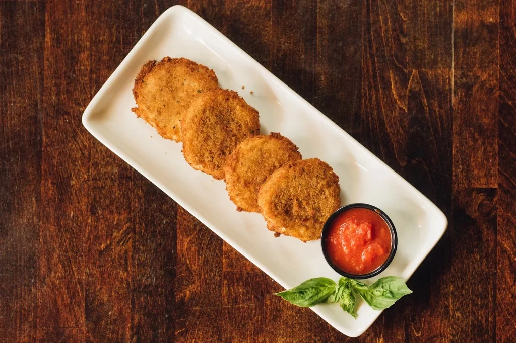 Five golden-brown fried items with red sauce and basil on a white plate.