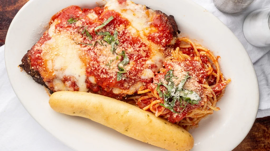 Parmigiana with spaghetti, red sauce, cheese, basil, and a breadstick.