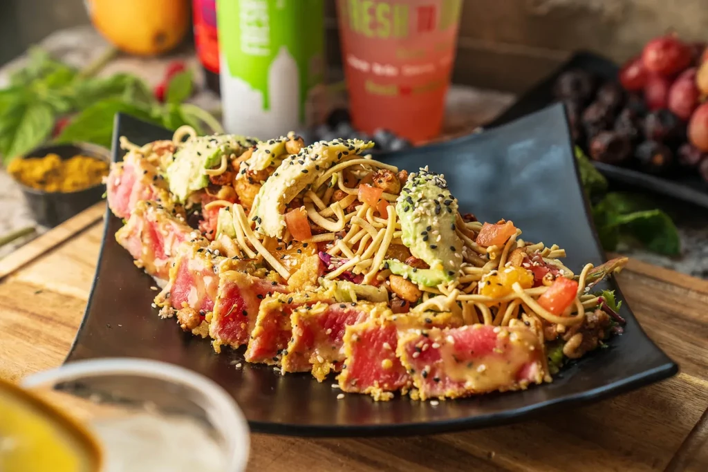 Seared tuna with sesame seeds, noodle salad, avocado, and fresh ingredients.