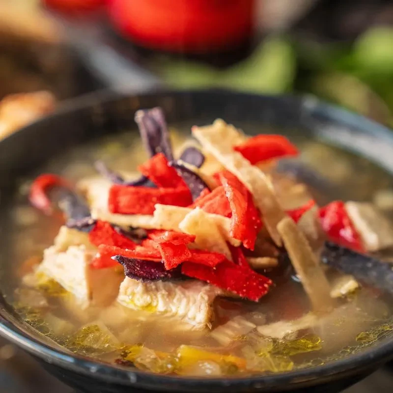 Close-up of clear-broth chicken soup with vivid tortilla strips.