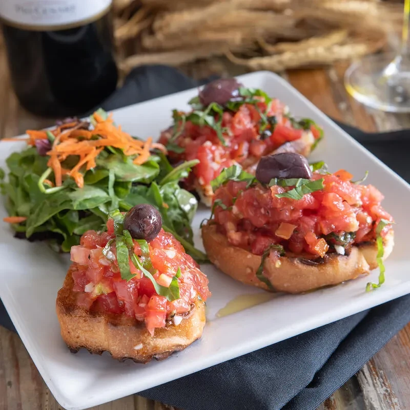 Toasted bruschetta with tomatoes, basil, olives, and a side salad.