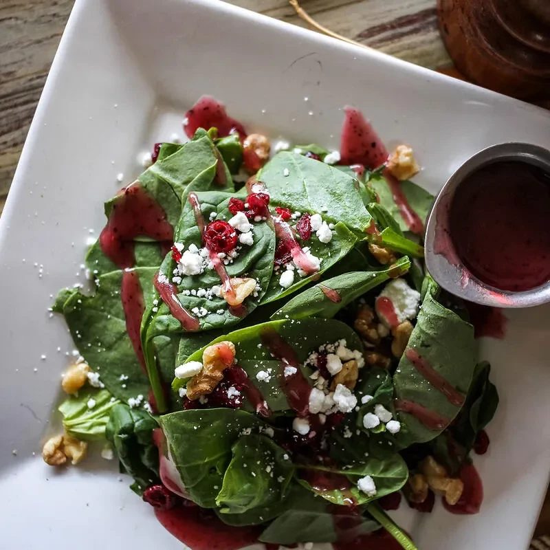 Salad with greens, cheese, walnuts, berries, and red dressing in white bowl.