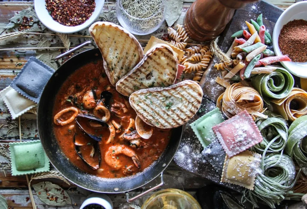 Overhead: Rustic Italian cioppino, grilled bread, uncooked pasta, spices.