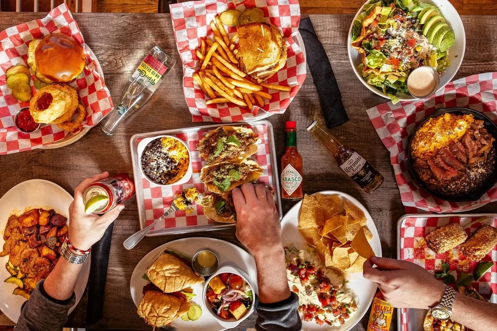 Overhead view: hands reaching for diverse food and drinks on a table.