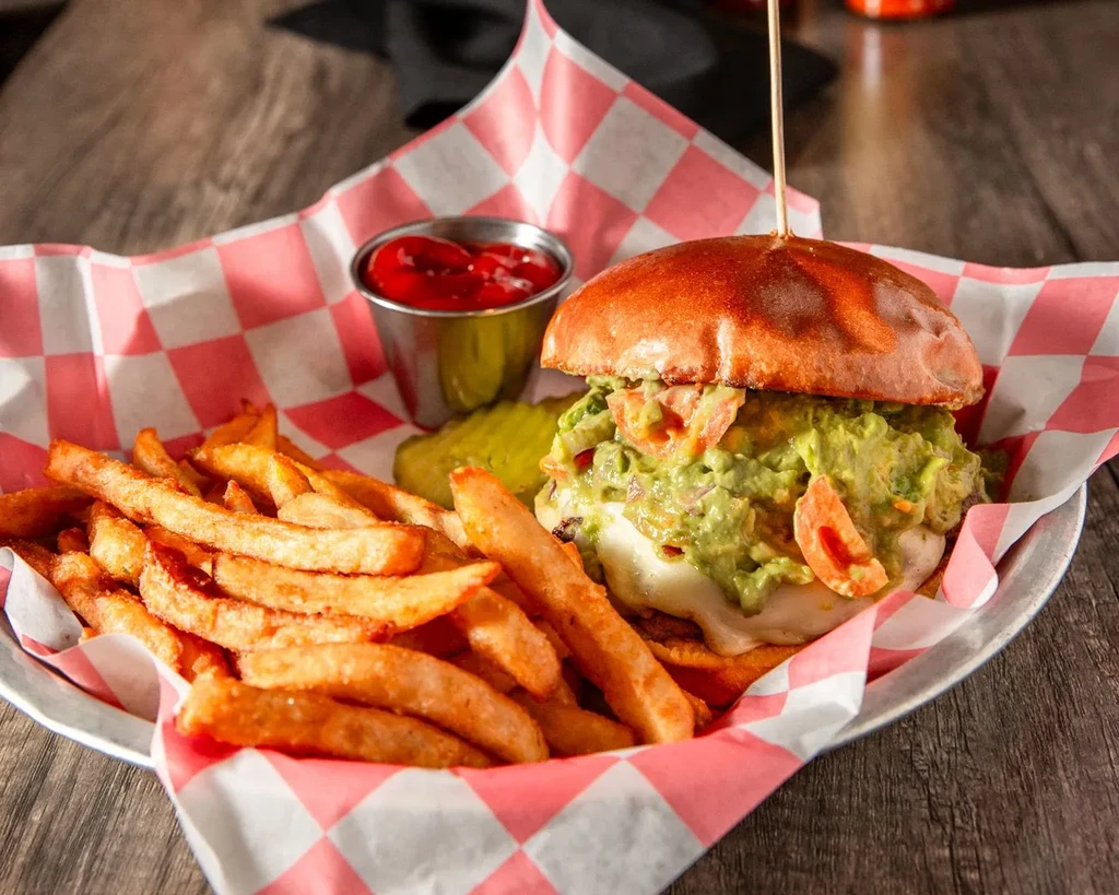 Gourmet guacamole burger with fries in a checkered diner basket.