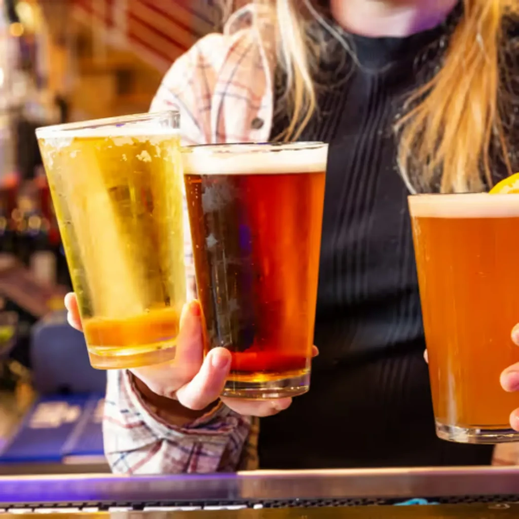 Three varying beers held by two people behind a bar.