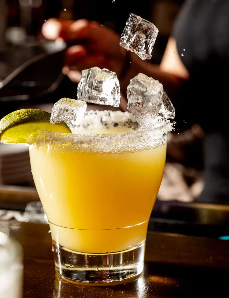 Yellow margarita with salt rim and lime, ice cubes falling.