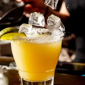 Dynamic close-up of a margarita with falling ice, salt rim, and lime.