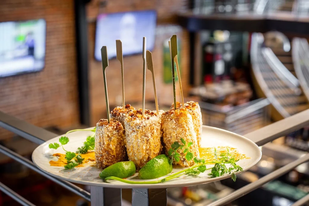 Elote segments with crumbly topping, cilantro, lime, and sauce on plate.