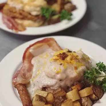 Two plates of biscuits and gravy, bacon, sausage, and potatoes.