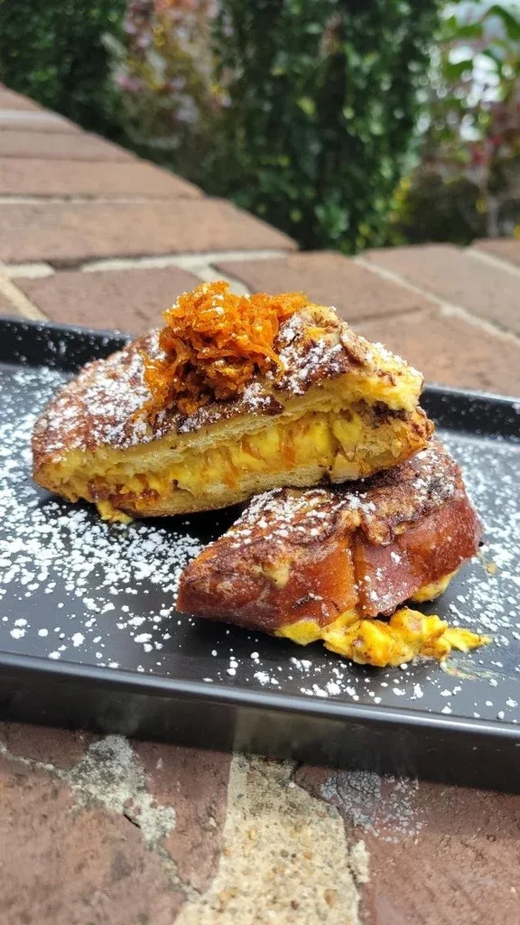 Sliced French toast with powdered sugar, orange zest on a black plate outdoors.