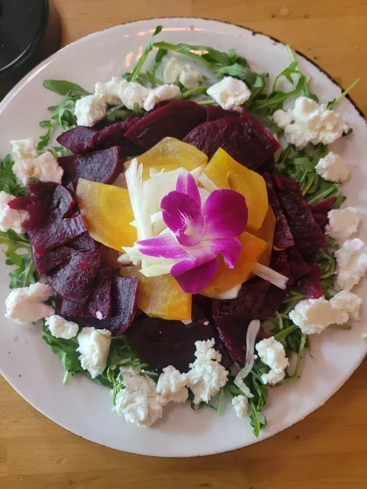 Colorful beet and goat cheese salad garnished with a purple orchid.