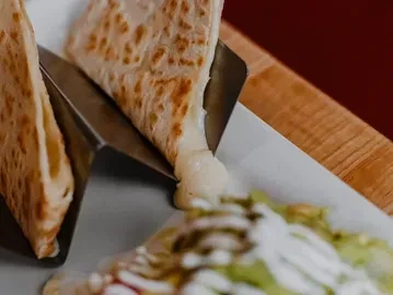 Triangular quesadilla wedge lifted, creating a long, melting cheese pull.