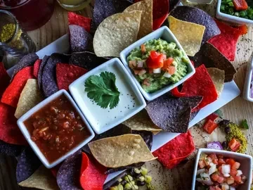Platter of multi-colored tortilla chips with salsa, guacamole, and other dips.