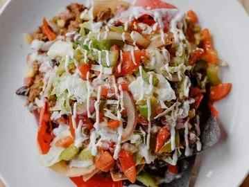 Top-down view of loaded nachos with meat, vegetables, and cream sauce.