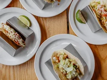 Multiple plates of garnished tacos with lime wedges on a wooden table.