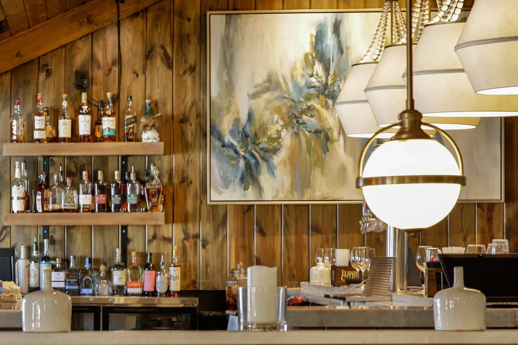 Rustic bar with stocked liquor shelves, abstract art, and modern lighting.