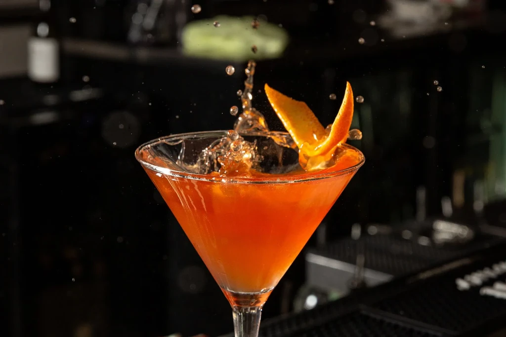 Orange cocktail in martini glass, splashing with a twisted orange peel.